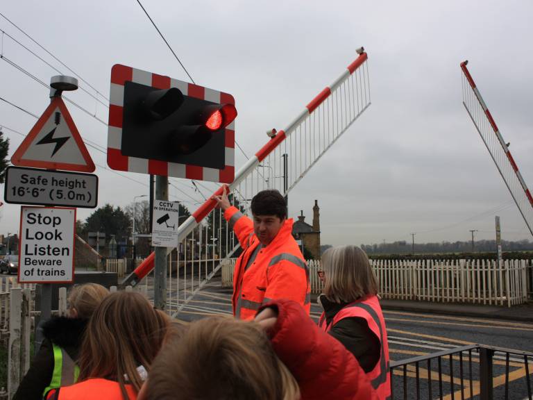 A photograph of a network rail staff member explaining the Foxton Level Crossing to a group of school children