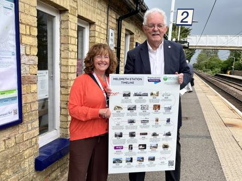 Photograph of Mike Lamport and Sarah Grove at Meldreth Station holding the Meldreth Station Historical timeline