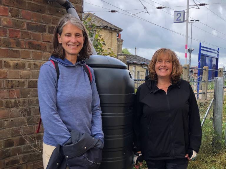 A photograph of Susan and Sarah standing in front of a water butt at Shepreth Station