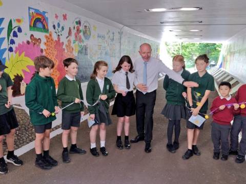 A line of school children holding a ribbon with the Police and Crime Commissioner opening the Meldreth Wonderpass