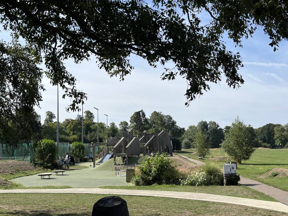 A photograph of Shelford Recreation Ground showing the play equipment in the foreground, and tennis courts and green space in the background.